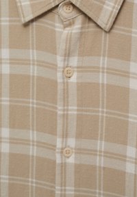 Camisa de cuadros beige y blanca con cuello y botones en la parte delantera, mostrando un primer plano de una tela de textura suave.