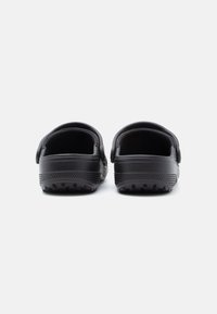 Pair of black slip-on clogs with textured soles viewed from the heel against a plain white background.
