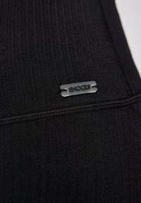 Zwarte ribstof met een gestructureerd oppervlak en een klein, grijs SNOCKS-label gestikt aan de naad. Minimalistisch ontwerp zonder extra details.