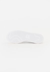 Hvid sneakersål med en tekstureret overflade, der har cirkulære og buede mønstre for greb og stabilitet. Flad og afrundet tådesign.