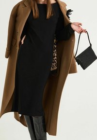 Abito midi nero con silhouette aderente, abbinato a un cappotto di lana marrone e a una borsa nera testurizzata. Dettaglio in stampa leopardata visibile all'interno del cappotto.