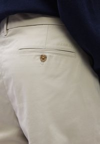 Μπεζ παντελόνι με λεία υφή, με πίσω τσέπη που κλείνει με στρογγυλό κουμπί. Το "Calvin Klein" είναι διακριτικά ανάγλυφο κοντά στην τσέπη.