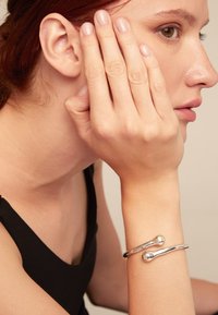 Bracelet en argent présentant un design lisse et arrondi avec deux accents sphériques. Porté au poignet d'une personne avec un arrière-plan neutre.