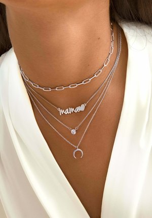Silberne geschichtete Halsketten mit einer Gliederkette, einem "Mama"-Anhänger, einem Edelstein und einem Halbmond, die alle an der Haut liegen.