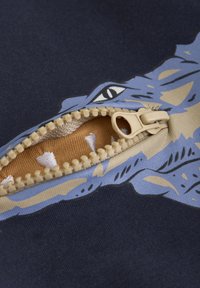 Marinblått tyg har en blå grafisk bild av en varg med beige detaljer. En beige dragkedja med en liten dragflik öppnas för att avslöja ett texturerat innertyg.