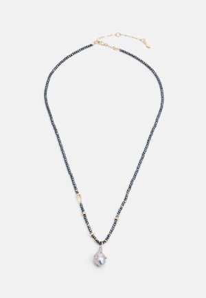 Halskæde med små mørke perler, guldaccents og en enkelt uregelmæssig hvid perle vedhæng på en hvid baggrund.