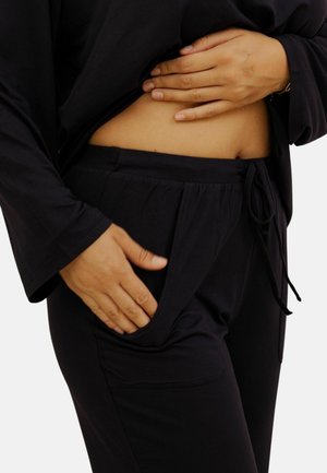 Ensemble de loungewear noir, comprenant un haut ample et un pantalon à cordon de serrage avec poches latérales. Tissu doux et texturé pour plus de confort.
