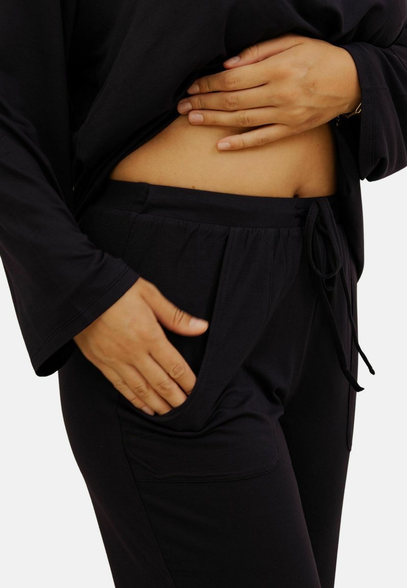 Ensemble de loungewear noir, comprenant un haut ample et un pantalon à cordon de serrage avec poches latérales. Tissu doux et texturé pour plus de confort.