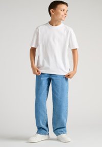 Camiseta blanca de algodón con mangas cortas, combinada con vaqueros azul claro y zapatillas blancas. Diseño sencillo, ajuste relajado.