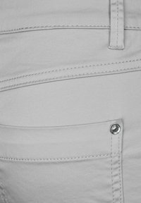 Jasnoszare dżinsy z małą kieszonką z srebrnym napem, kontrastowym przeszyciem i gładką fakturą.