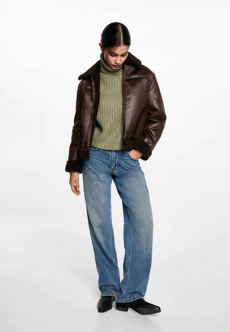 Jachetă din piele maro cu trimuri de blană neagră, pulover verde cu guler înalt cu nervuri și blugi largi de culoare albastru deschis. Botine negre la glezna completează ținuta.