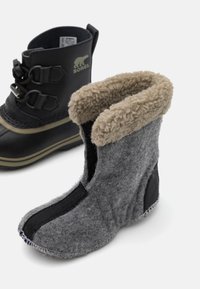 Svart vanntett støvel med snøring og gummisåle ved siden av grå filtstøvel med beige fleece-fôr og kontrasterende svarte detaljer.