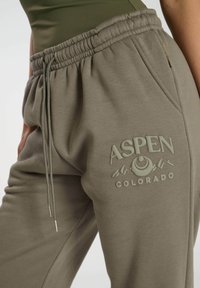 Olivgrön sweatpants med dragsko i midjan, med en upphöjd logotyp av "ASPEN COLORADO" och bergsgrafik på vänster lår.