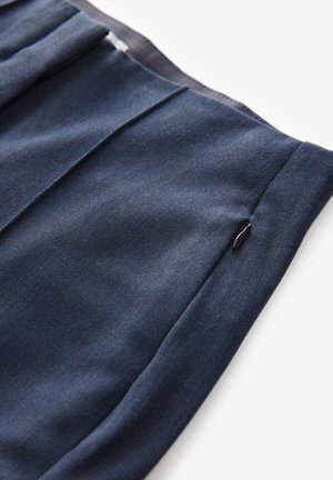 Sinih sinet fabric dengan tekstur halus dan detail jahitan diagonal. Memiliki saku resleting tersembunyi, menunjukkan desain yang bersih dan terukur.