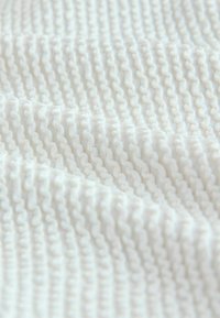 Biały tkanina o fakturze z wypukłym, falistym wzorem, prezentująca falujące fałdy i miękkie, gładkie wykończenie na całej powierzchni.