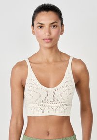 Bralette de ganchillo en blanco roto con escote profundo, patrones texturizados y tirantes anchos. Presenta un estilo ajustado y recortado.