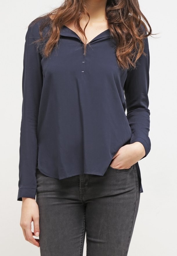 Camicia a maniche lunghe di colore navy con collo classico, tre bottoni e orlo leggermente curvo. Tessuto liscio, abbinata a jeans scuri.