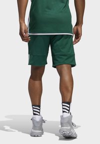 Grüne Sportshorts mit lockerer Passform, versehen mit weißen Seitenstreifen, kombiniert mit grauen Sportschuhen und schwarz-weißen gestreiften Socken.