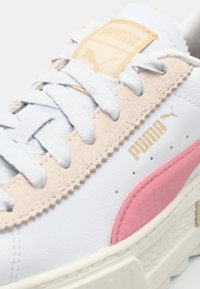 Valged tennisjalatsid roosa ja beeži sukidetailiga, tekstuursete pindadega, sidumissegmendiga disain ja kuldse logodetailiga keelega.
