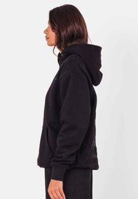 Zwarte capuchontrui, gemaakt van een zachte katoenmix. Heeft een comfortabele, losse pasvorm, een kangoeroezak en geribbelde manchetten voor extra draagcomfort.