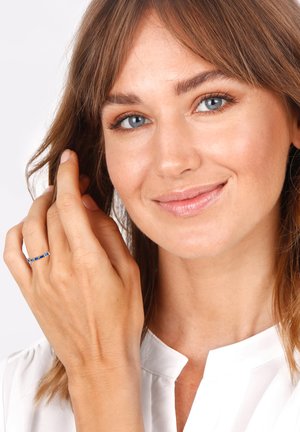 Silver band ring featuring blue rectangular stones, held by a hand. Smooth texture, set against a light background.