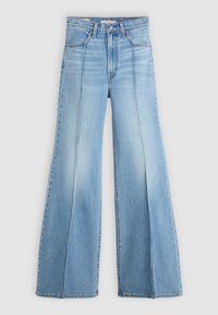 Jean denim bleu clair taille haute avec jambes larges évasées et détails de couture devant sur un fond uni.