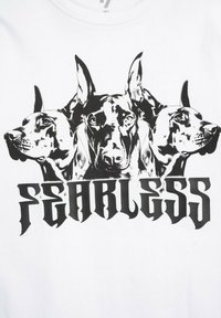 Biała koszulka z czarną grafiką trzech głów dobermanów nad słowem "FEARLESS" w pogrubionej, stylizowanej czcionce.
