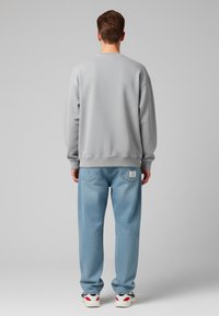 Felpa grigia con spalle scese, abbinata a jeans baggy azzurri. Presenta polsini a costine e una patta sul retro dei jeans. Sneakers bianche.