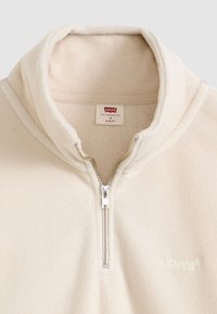 Ζακέτα από φλις σε κρεμ απόχρωση με ψηλό γιακά, με μερικό φερμουάρ στο μπροστινό μέρος και υφή, με διακριτικό κεντημένο λογότυπο στο στήθος.