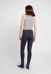 Jeans oscuros ajustados combinados con una camiseta sin mangas a rayas blancas y marinas, y zapatillas altas azules, vistas desde la parte de atrás.