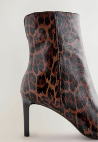 Leopard print heeled ankle boot, featuring a textured surface, black accents, and a sleek, fitted silhouette with a pointed toe.