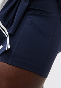 Κοντινό πλάνο στο μηρό σκουρόχρωμου δέρματος που φοράει σκούρο μπλε αθλητικό σορτς με ορατή πλαϊνή τσέπη και ραμμένες ραφές.