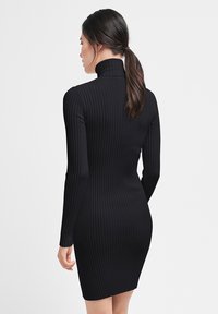 Schwarzes, geripptes Langarmkleid mit hohem Kragen. Figurbetontes Design, bis zur Mitte des Oberschenkels und glatte Textur. Minimalistischer Stil ohne Verzierungen.