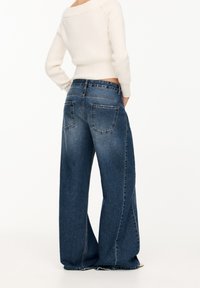 Wide-leg blue denim jeans featuring a mid-rise waist, contrasting stitching, and two back pockets. The fabric has a smooth texture.