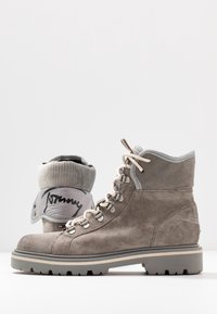 Botas de senderismo de ante gris con suelas gruesas y cordones blancos, una bota doblada en la parte superior que muestra un logotipo en el interior del collar.