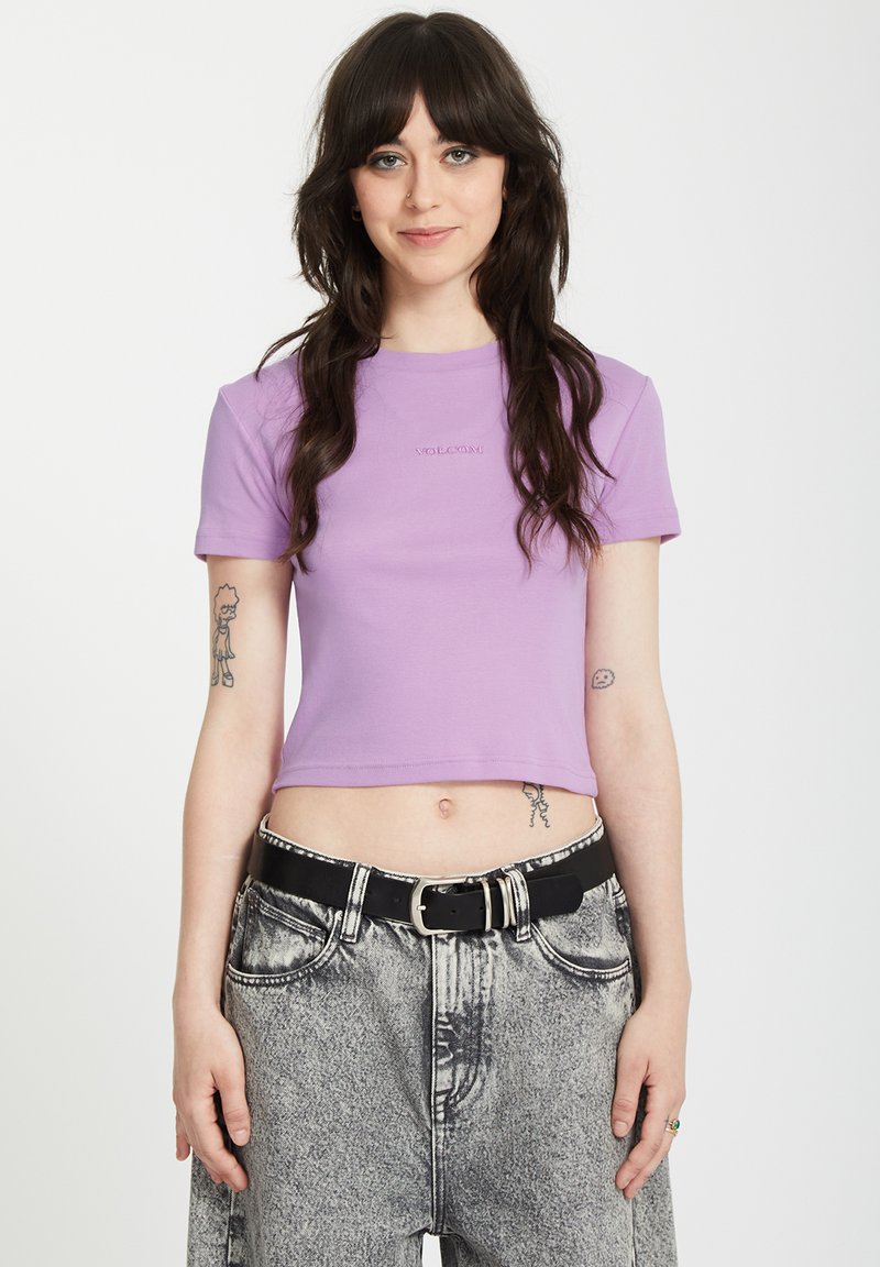 Paarse cropped t-shirt met korte mouwen. Heeft een subtiele logo op de borst en wordt gecombineerd met hoge taille, acid-wash jeans en een zwarte riem.