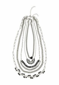 Ogrlica u srebrnoj boji s više slojeva lanaca različitih stilova, sadrži crne perle i akcentne detalje, različitih dužina, i glatku teksturu.