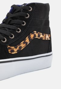 Černý vysoký tenisky vyrobené z plátna, s akcentem v leopardím vzoru a kontrastní bílou podrážkou s černým obvodem.