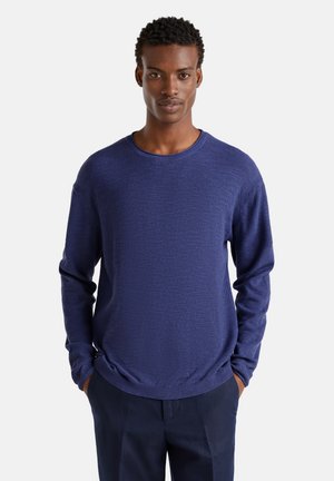 Navyblaue, strukturierte Strickjacke mit langen Ärmeln und Rundhalsausschnitt; lockere Passform mit gerippten Bündchen und Saum. Trägt man mit Händen in den Taschen.