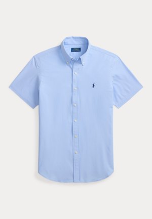Camisa azul clara de manga corta con botones, cuello abotonado y pequeño logo oscuro bordado en el pecho izquierdo.