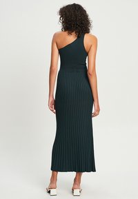 Dunkelgrünes, geripptes Midikleid mit einem Schulterträger, tailliertem Oberteil und schwingendem, gefaltetem Rock. Hergestellt aus elastischem Material.