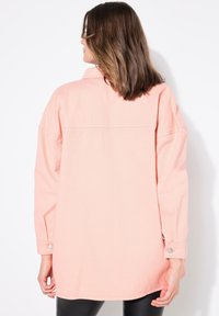 Camisa de algodón de gran tamaño en color durazno, con mangas largas, puños abotonados y una costura en el yugo trasero, que presenta un ajuste relajado y una textura suave.