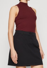 Burgundy ribbad ärmlös topp med hög halsringning, tillsammans med en svart minikjol med knappstängning och sidofickor.