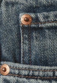 Blaue Denim-Jeans-Tasche mit Kupfernieten und braunen Nähten, Nahaufnahme der Textur und Nähdetails.