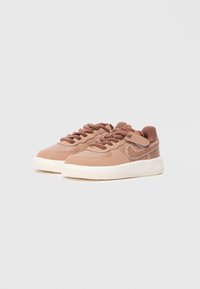 Rózsaszín bőr sportcipők texturált barna fűzőkkel, fehér gumitalppal és ezüst színű díszvarrással az oldali logón. Lekerekített orr kialakítás.