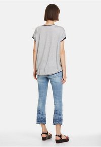 Gray short-sleeve shirt with navy accents, paired with light blue cropped jeans featuring embroidered details at the hem and black sandals.