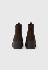 Bottines en suede marron avec un talon noir épais, des panneaux élastiques sur les côtés et des languettes à l'arrière pour un enfilage facile.