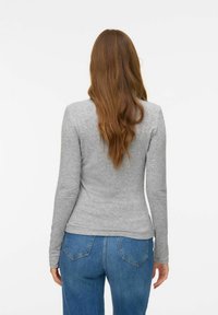 Grijze top met lange mouwen en een aangesloten ontwerp, gemaakt van zacht katoen. Gecombineerd met blauwe high-waisted jeans, die een casual stijl tonen.