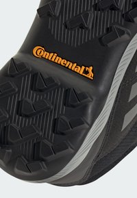 Black shoe sole with textured grip pattern, featuring a prominent orange "Continental" logo and gray accents along the edge.