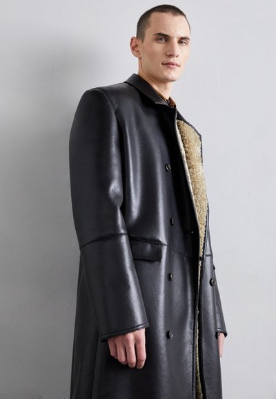 Black leather coat with a double-breasted design, featuring a textured, beige shearling lining and side pockets. Smooth finish.